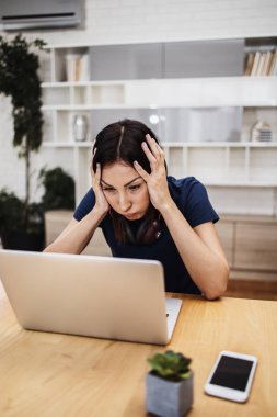 Yorgun ve yorgun orta yaşlı kadın serbest çalışıyor ve evinde çalışıyor. Arka planda modern oturma odası. Serbest meslek kavramı.