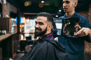 Yakışıklı bir genç adam saç ve sakal stili yaptırıyor ve profesyonel kuaför tarafından giydiriliyor..