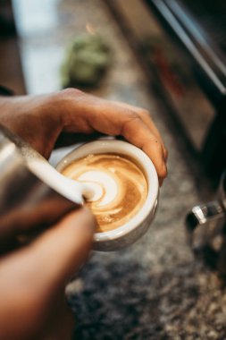 Deneyimli barmen ellerinin taze espresso kahve ya da kapuçinonun içine sıcak süt döktüğü yakın çekim. Latte sanat konsepti. 