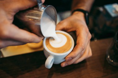 Deneyimli barmen ellerinin taze espresso kahve ya da kapuçinonun içine sıcak süt döktüğü yakın çekim. Latte sanat konsepti. 