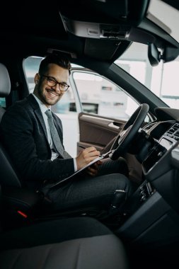 Galeride çalışan araba satıcısı ve araba detaylarını son kez kontrol ediyor alıcı gelmeden önce..