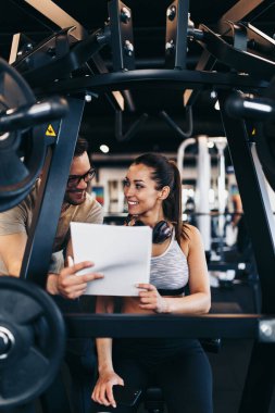 Modern spor salonunda spor yapan genç ve çekici bir kadın. Kişisel fitness hocası veya koçuyla birlikte..