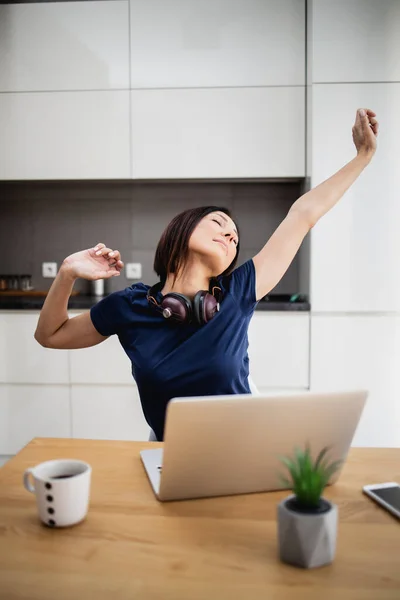 Attractive and happy middle age female freelancer is working and smiling at her home. Modern kitchen in background. Freelancing job concept.