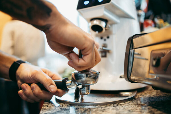 Крупный план профессионального бармена, готовящего кофе эспрессо в эксклюзивном кафе-баре или кафетерии. Он использует кофемолку или мельницу.