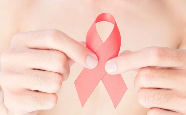 Hand hält rotes Band mit verschwommenem Hintergrund für Aids-Aufklärungskonzept — Stockfoto