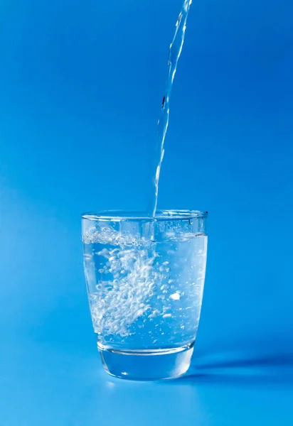 Verter agua en un vaso sobre fondo azul — Foto de Stock