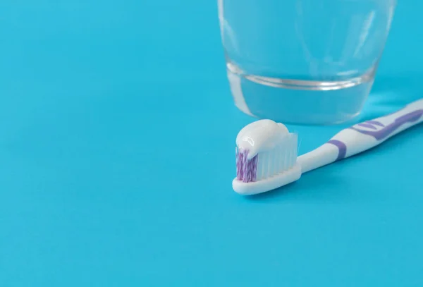 Primeros planos de pasta de dientes en cepillo de dientes con vaso de agua en azul backgr — Foto de Stock