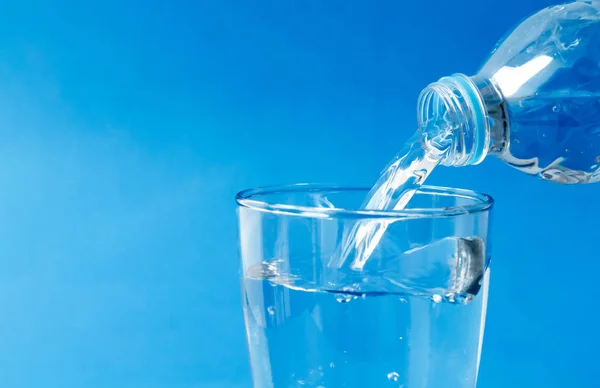 Наливание воды в стекло на голубом фоне — стоковое фото