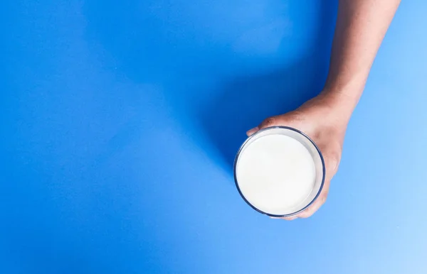 Hand met glas melk op blauwe achtergrond, eten en drinken voor gezonde concept — Stockfoto