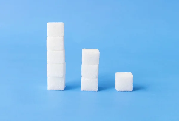 Montones altos a bajos de terrones de azúcar con fondo azul, concepto de cuidado de la salud — Foto de Stock