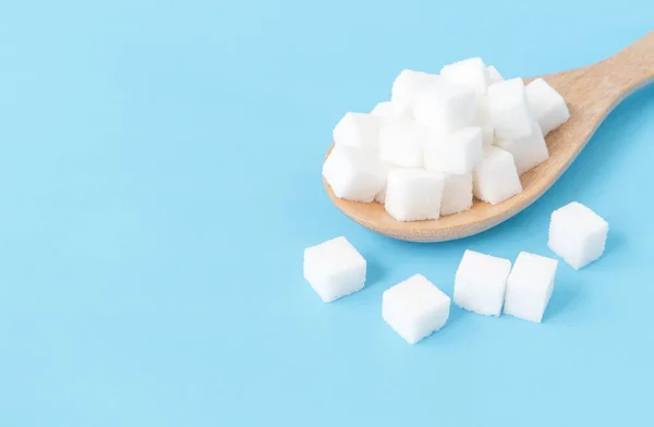 Closeup sugar cubes on wood spoon white blue background — Stok Foto