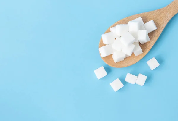 Closeup top view sugar cubes on wooden spoon white blue background — Stock Photo, Image