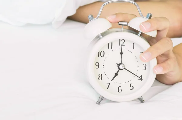 Closeup woman hand turn off alarm clock on white bed in the morning for wake up time concept Stock Picture