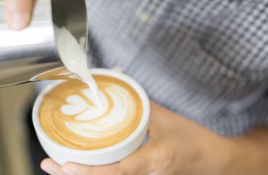 Woman barista pouring stream milk for making latte art coffee with tulip shape in white cup, selective and soft focus clipart
