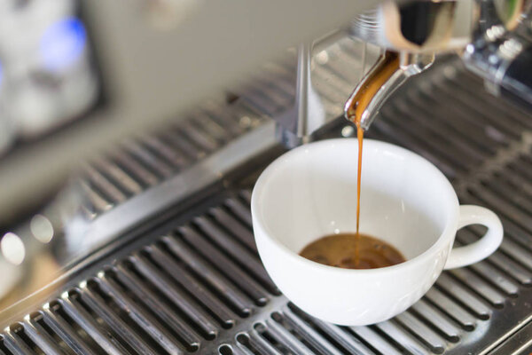 Closeup espresso pouring to white cup from coffee machine, selective and soft focus