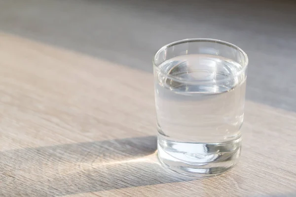 Bicchiere d'acqua sul tavolo in legno con luce al mattino, concetto di cura sana, messa a fuoco selettiva — Foto Stock