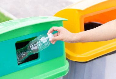 Çöp plastik şişeyi geri dönüşüm çöp kutusuna tutarak el ele kapama, seçici odak