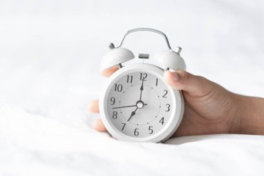 Kapalı el beyaz yatakta çalar saati tutuyor, uyanma zamanı.