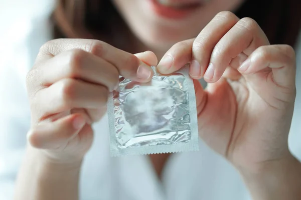 Close up mão mulher segurando preservativo deitado na cama branca, cuidados de saúde e conceito médico — Fotografia de Stock