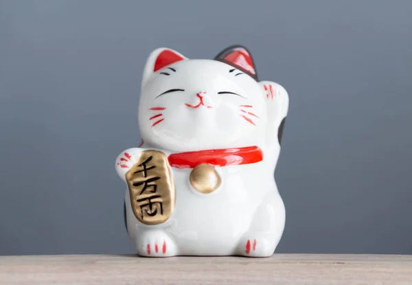 Maneki neko lycklig katt visa text på handen vilket innebär rik på trä bord bakgrund, välj fokus — Stockfoto