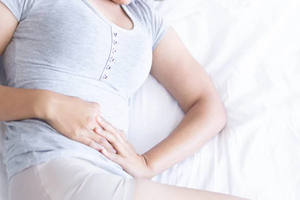 Gros plan femme maux d'estomac couché sur un lit blanc, concept de soins de santé, accent sélectif — Photo