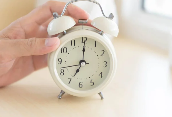 Mão de close-up segurando despertador na mesa no quarto, hora de acordar — Fotografia de Stock