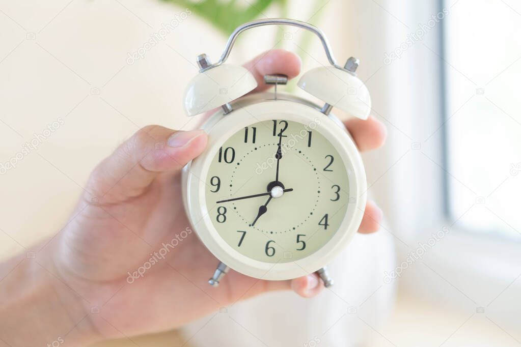 Closeup hand holding alarm clock on table in bedroom, Time to wake up