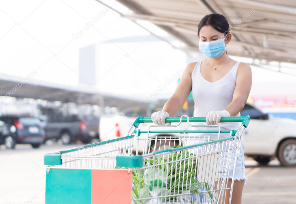 Closeup woman wearing face mask for protect air polution or virus covid 19 with shopping cart in supper market, selective focus
