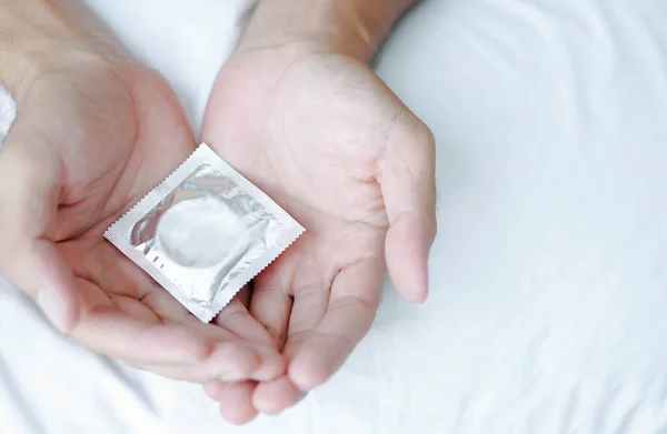 Close Homem Mão Segurando Preservativo Deitado Cama Branca Cuidados Saúde — Fotografia de Stock