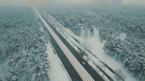 Arabalar ve tramvay ile kış orman yolda üstten görünüm yukarıda. Kar yağışı hava dron görüntüleri — Stok video
