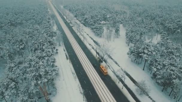 Von oben auf der winterlichen Waldstraße mit Autos und Straßenbahn. Schneefall aus der Luft Drohnenaufnahmen — Stockvideo