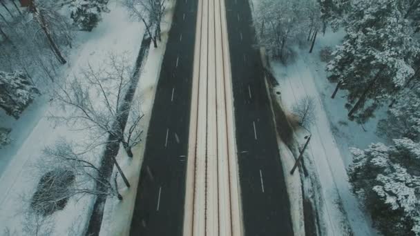Πάνω από το top view στο χειμερινό δασικό δρόμο με τα αυτοκίνητα και τα τραμ. Χιονόπτωση τον εναέριο κηφήνα πλάνα — Αρχείο Βίντεο