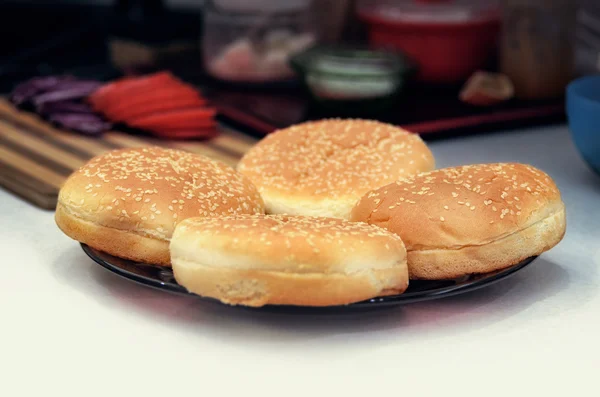 Čtyři housky se sezamovými semínky pro hamburgery na štítku na kuchyňském stole. Vaření burger koncepce — Stock fotografie