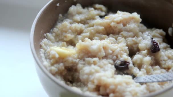 Porridge with banana and raisins. Oatmeal in deep dish with big spoon — Stock Video