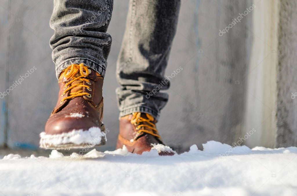 Man walks in the snow street. Feet shod in brown winter boots. Winter walks concept