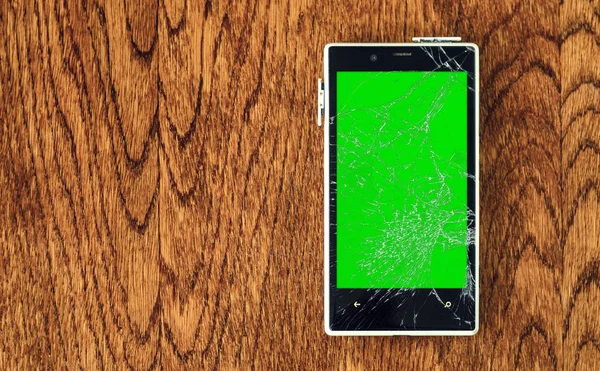 Smartphone with broken screen on wooden table.