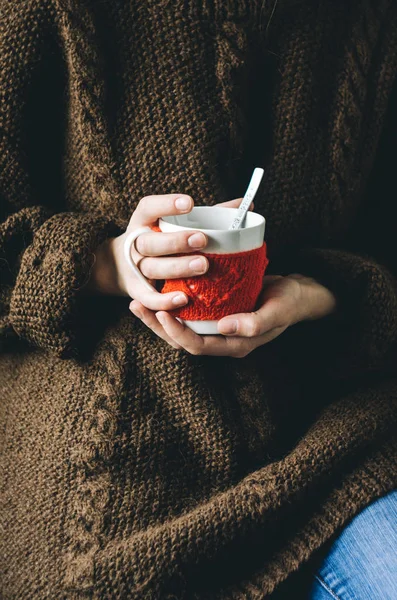 Red Knitted woolen cup with heart pattern in female hands.