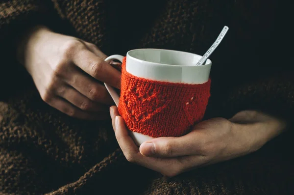 Red Knitted woolen cup with heart pattern in female hands.
