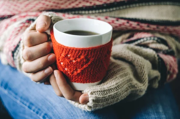 Red Knitted woolen cup with heart pattern in female hands.