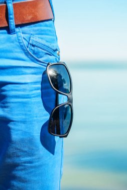 Güneş gözlüğü açık cebinden kot yakın çekim asılı. Güneşli bir gün sahilde, deniz arka plan üzerine yaz gardırop parçası