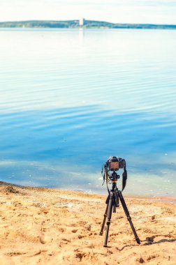 Bir kamera bir tripod üzerinde kum sahil deniz manzarası kaldırır. Manzara çekim sürecinde fotoğrafik donanımlar. Kamera fotoğraf çekerken veya hızlandırılmış