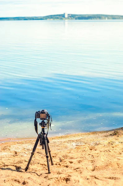 Bir kamera bir tripod üzerinde kum sahil deniz manzarası kaldırır. Manzara çekim sürecinde fotoğrafik donanımlar. Kamera fotoğraf çekerken veya hızlandırılmış