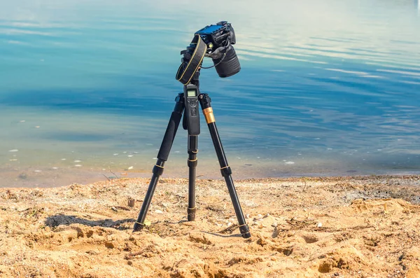 Deniz kum üzerinde deniz kıyısına yakın bir tripod üzerinde kamera kaldırır. Manzara çekim sürecinde fotoğrafik donanımlar. Kamera fotoğraf çekerken veya hızlandırılmış