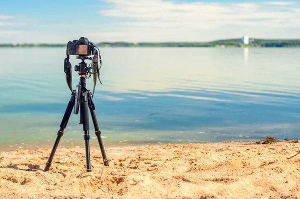 Bir kamera bir tripod üzerinde kum sahil deniz manzarası kaldırır. Manzara çekim sürecinde fotoğrafik donanımlar. Kamera fotoğraf çekerken veya hızlandırılmış