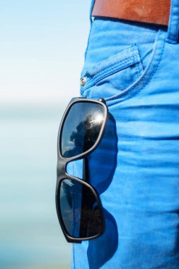 Güneş gözlüğü açık cebinden kot yakın çekim asılı. Güneşli bir gün sahilde, deniz arka plan üzerine yaz gardırop parçası