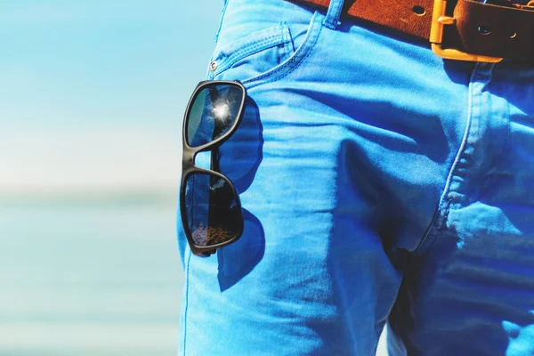 フロント ポケットのブルー ジーンズのクローズ アップに掛かっているサングラス ビーチ 海の背景に夏のワードローブの一部で晴れた日 — ストック写真
