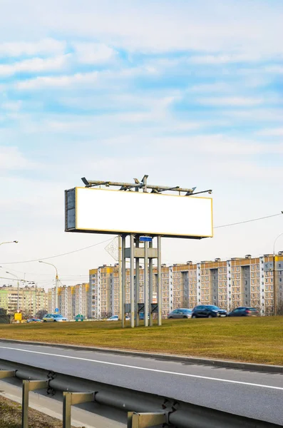 Blank white billboard on the highway with passing cars on the background of multi-storey city buildings, mock up