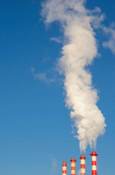 stock image Plant pipes with smoke against clear blue sky.