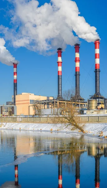 Thermal power plant during winter operation on the river bank. High chimneys emit a large amount of smoke