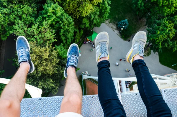 Feet Hanging in the Air First Person View. Above the City Park. Two People Riding a Ferris Wheel Top View